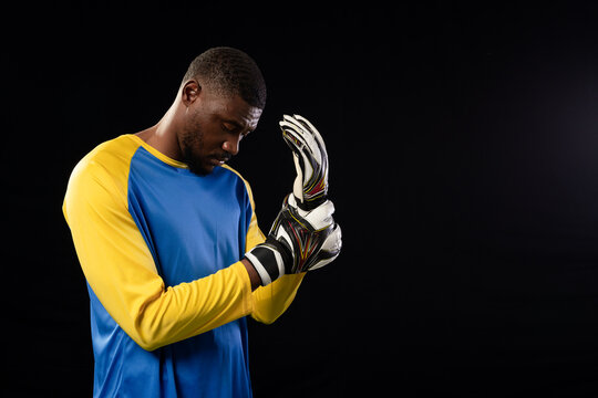 Mid-adult man adjusting padded goalie gloves with straps while wearing blue yellow jersey in studio