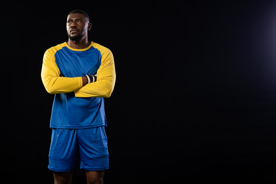 Mid-adult man standing with arms crossed in studio wearing blue jersey and wrist tape, copy space