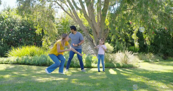 Family in yard, mother beginning blowing with wand, father guiding child to pop bubbles