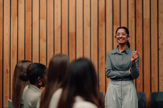 Professional woman smiling, delivering presentation to audience, sharing knowledge at business seminar