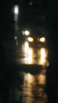 A moody scene of car headlights creating a bokeh effect in the rain. Warm light reflects off the wet asphalt. A dark, atmospheric scene with a cinematic feel, perfect for conceptual use