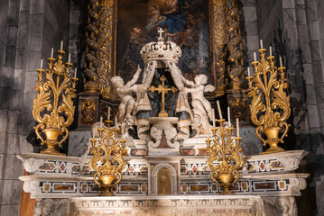 Fototapeta premium Ornate Baroque altar in Menton, France, with two angels raising a crown above a crucifix, gilded candlesticks, tall framed painting, and warm lighting on marble and gold