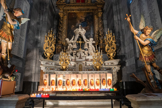 Baroque church altar in Menton, France, shows a marble tabernacle with a crown, gilded candlesticks, polychrome archangel statues, candles, and a large painting.