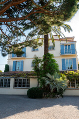 Cream walled villa in Antibes, France stands behind palms and vines, with wrought iron balconies, tiled roof, and paned windows in bright daylight and crisp shadows. © Aerial Film Studio