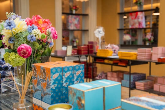 Warm boutique in Grasse, France presents pastel gift boxes, floral displays, reed diffusers, and perfume items on black tables and shelves with turquoise gold accents.