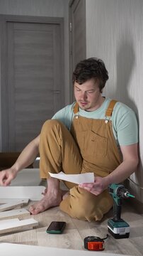Confused handyman sitting on the floor, experiencing difficulty and stress while reading the complex instructions for assembling flat-pack furniture, feeling puzzled and overwhelmed
