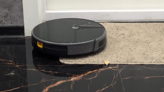 Robot vacuum cleaner works on floor near door mat to remove dirt and debris in home setting