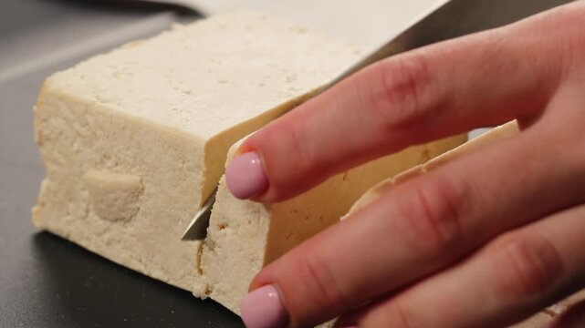 Chef cut cheese for Fried tofu with sesame seeds and spices on cast iron pan, cooking japanese salad. Healthy ingredient for cooking vegan vegetarian diet food. Roasted tofu over black background.