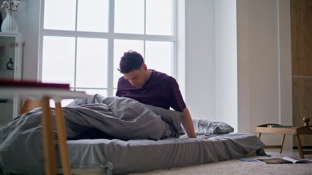 Stressed man awaking early morning. Tired guy feeling exhausted going mattress