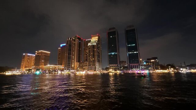 CAIRO, EGYPT - APRIL 2026: Night time-lapse (hyperlapse) over the River Nile showing illuminated party boats passing by the bright city skyline and the prominent Nile City Towers.