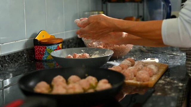 Homemade meatballs batch cooking in rustic kitchen, female hands preparing more raw meatballs for family meal preparation, traditional meat recipe process