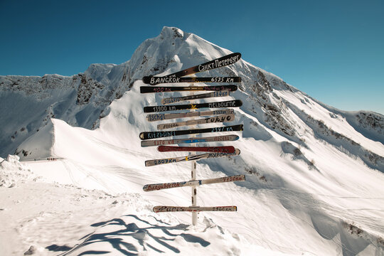 Signposts Mark Distances to Various Cities With a Snowy Mountain Backdrop in Bright Sunlight
