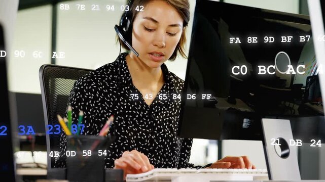 Call agent typing and helping client, headset on, peer handing papers, hex animating over monitor