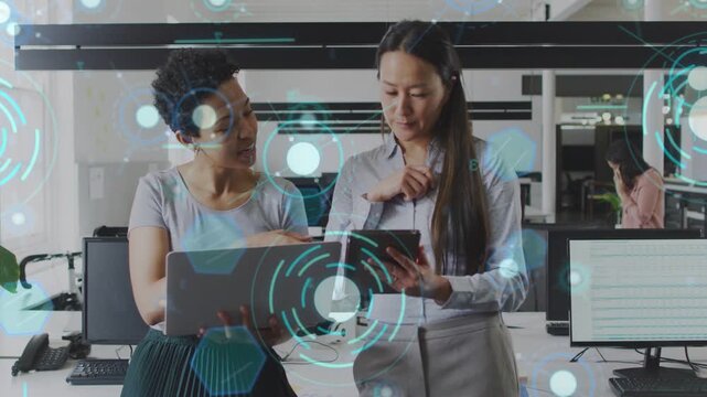 Left woman showing laptop peer checking business data and tapping tablet agreeing while HUD pulses