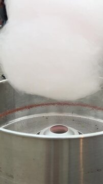 Vertical video close up. Seller behind street sweets counter, stall makes and sells white cotton candy in machine. Concept of city festival Tbilisoba, fair, sale, sugary, pastry shop, street market