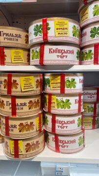 Assorted round boxes of the famous Roshen Kyiv Cake and Grillage Cake with their signature chestnut leaf design on shelves in a local grocery store in Kyiv.