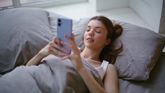 Woman morning scrolling mobile phone lying in bed closeup. Girl reading message
