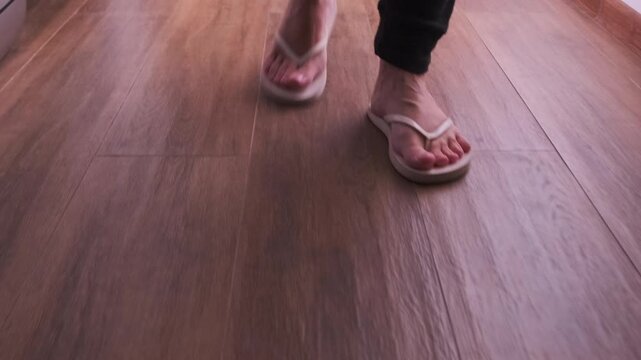 Front view of female footsteps in flip-flops walking down a dark hallway, showing movement, barefoot style footwear, indoor floor texture, casual motion, close-up leg action and step rhythm
