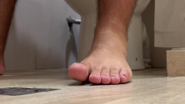 Horizontal video close up. 60 fps. White naked man sits on toilet in public WC, hotel bath room, apartment, hostel. Bare male hairy legs without pedicure. Problems with diarrhea, intestines, clean