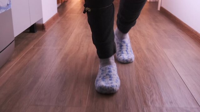 Front view of female steps in woolen socks walking down a dark hallway, showing soft indoor movement, cozy footwear, floor texture, casual home activity, close-up leg motion and step rhythm