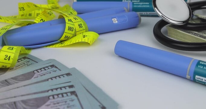 Camera traveling over money and Semaglutide injection pens with a black stethoscope and measuring tape on a white background.