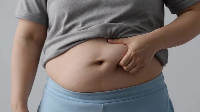 Close-up of person in casual clothing examining abdominal fat, expressing concern about weight management and health awareness.