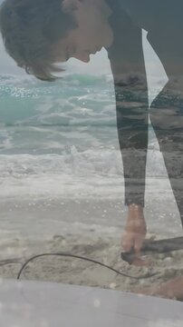 Vertical video: Surfer grabbing leash and securing plug on surfboard while waves layering frame