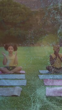 Vertical video: Two kids cued on mats, lifting, clapping, joining for health, wisps drifting around