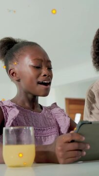 Vertical video: Mom leaning, kid tapping tablet, using learning app, juice glass and sparkles over