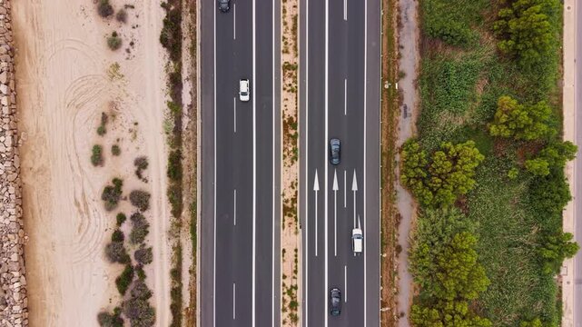 Overhead top-down view of a multi-lane divided highway with cars traveling in both directions, flanked by sandy desert terrain and green shrubs