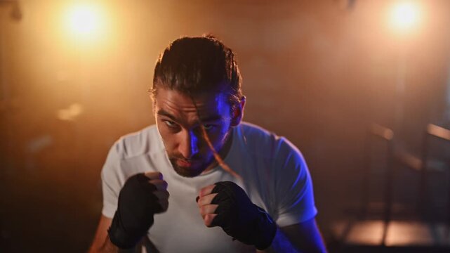 Focused martial artist shadow boxing in a hazy, backlit gym while practicing powerful punches and defensive moves in slow motion