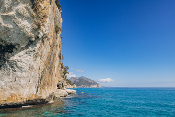 Fototapeta premium Dramatic sea cliff rock formation meeting turquoise water on a sunny day in Gulf of Orosei, Sardinia, Italy