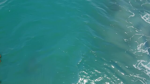 Aerial view of clear turquoise water with light patterns reflecting on the surface, showcasing gentle waves and ripples in a serene coastal environment