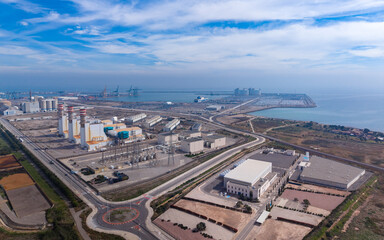 Fototapeta premium Aerial view of large coastal industrial complex featuring a combined cycle gas power plant, water distillation station, electrical substation, and commercial seaport with cranes along the Mediterranea