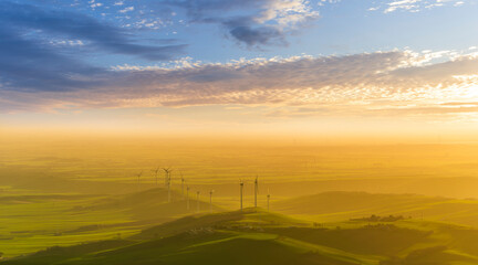Obraz premium scenic landscape of gloden evening sunset in beautiful rural valley with amazing hills and fields and wind turbines of power plant stations with awesome clousy sky on background