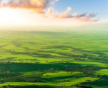 panoramic view of green sunset or sunrise valley with agricultural fields and hills with roads leading far to horizon and beautiful clousy evening sky