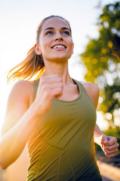 Happy young woman in green sportswear running through a sunlit park during golden hour, embodying a sense of pure endorphin release, vitality, and physical liberation while training outdoors.