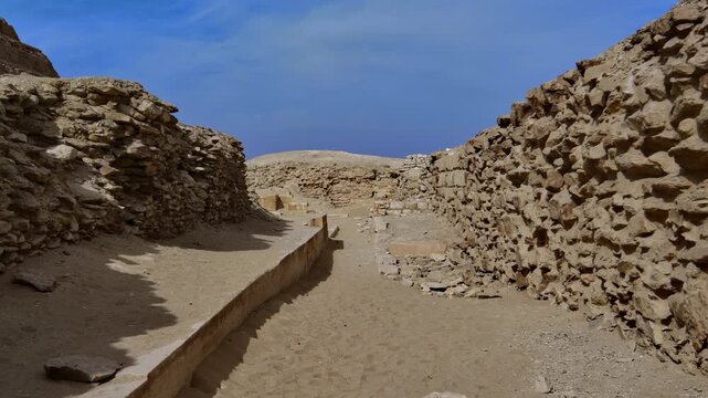 Step Pyramid of Djoser at Saqqara necropolis, Egypt, world's oldest pyramid with surrounding ancient ruins, stone blocks and arched entrance wall under blue sky.