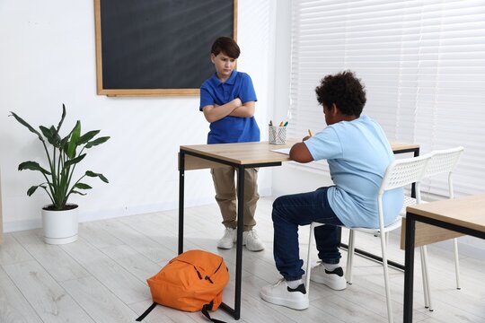 Boy bullying his African American classmate in classroom