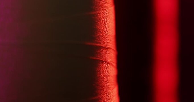 Macro shot of a dark thread spool with a needle. The scene changes to hanging metallic handles with rivets. Both clips feature abstract, vibrant purple and pink lighting.