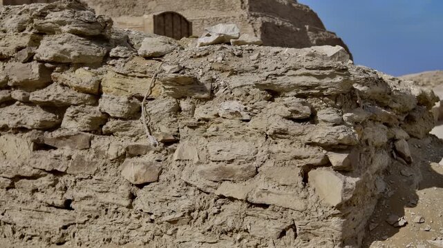 Ground level view of Step Pyramid of Djoser at Saqqara, Egypt, tiered limestone structure with ancient ruined entrance pavilion and stone foundations.