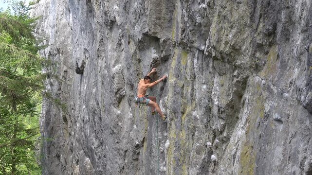 Male rock climber moves smoothly while lead climbing a rugged limestone face, stretching for the next hold. Strong, focused and agile young athlete during a sport climbing session on a warm summer day