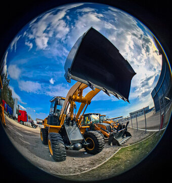 Powerful yellow front loader with bucket raised captured under bright cloudy sky at construction site using fisheye lens