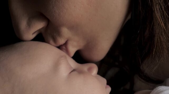 Close up loving mother gently kissing forehead of sleeping newborn baby. Family unbreakable bond between parent and child, motherhood and beauty of infancy. Mother showing her love to newborn
