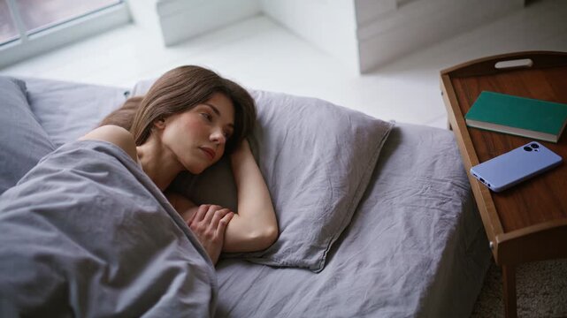 Closeup brunette sleeping pillow checking cellphone clock. Woman snoozing alarm