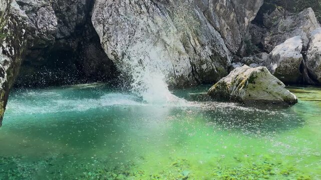 Young man jumps into the crystal clear emerald water of the pristine Soca River in Slovenia. Sunlit rocks, fresh alpine water, and a peaceful canyon setting create an adventurous summer holiday scene.