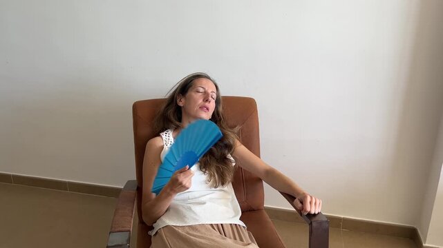 Mujer abanic&aacute;ndose frente al ventilador por sofocos de la menopausia