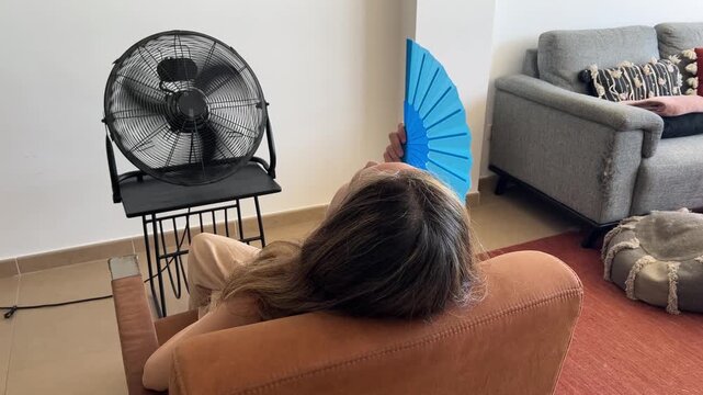 Mujer con sofocos frente al ventilador abanic&aacute;ndose, vista trasera