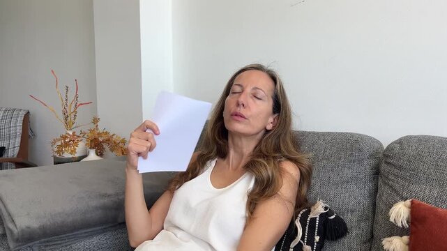 Mujer sudando por sofocos de la menopausia abanic&aacute;ndose con un papel