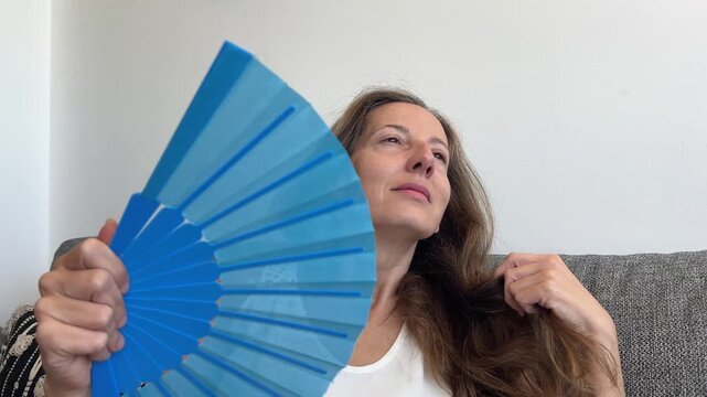 Mujer abanic&aacute;ndose con abanico azul para aliviar sofocos de la menopausia